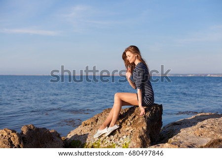 the girl in the striped dress sits on the rocks by the sea