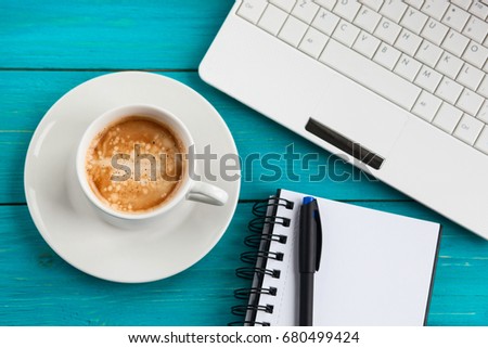 Office items with cup of coffee, notebook, pencil and laptop on a blue turquoise table