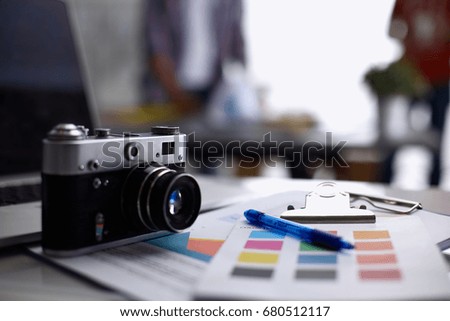 Laptop and camera on the desk, two businesspeople standing in the background
