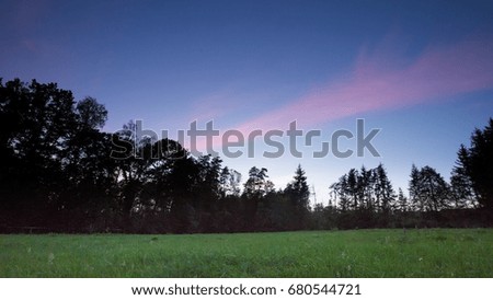 After sunset sky over meadow and forest. Romantic landscape.