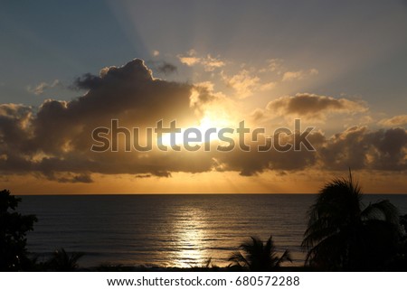 Sun behind the cloud at dusk and its reflexion over the calm ocean surface