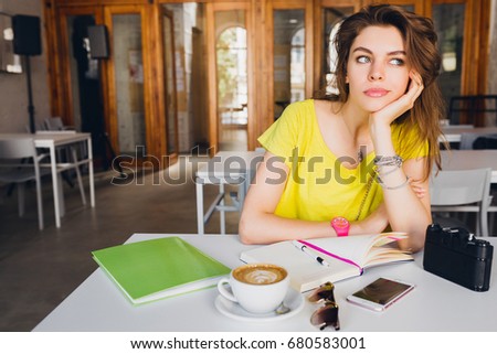 young beautiful hipster woman sitting at table in co-working office, summer outfit, diary, bored, thinking, sad, working