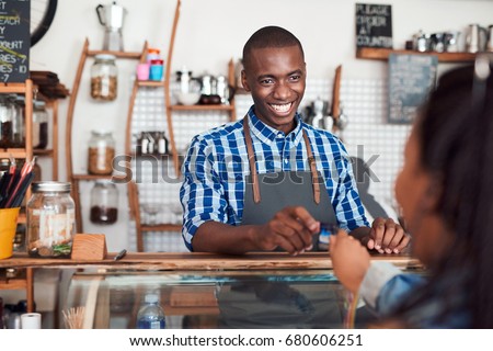 Smiling barista standing behind a counter in a cafe taking a credit card from a customer to pay for her purchase