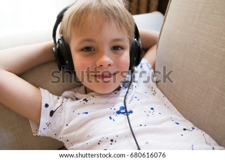 small cute boy seats on the bed and listening music with earphones and have rest and relax