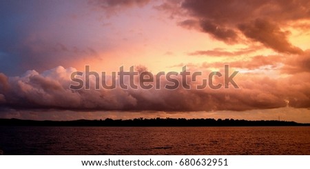 Orange ocean sunset with stormy back-lit stratocumulus clouds and water reflections. Highlighted low level cloud bank at sea looking toward land. Skyscape nature background
Australian  East Coast.

