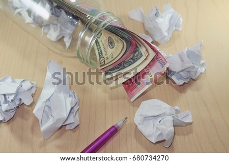 Various money currency from glass jar, crumpled paper and pen on wood table, idea and savings concept  