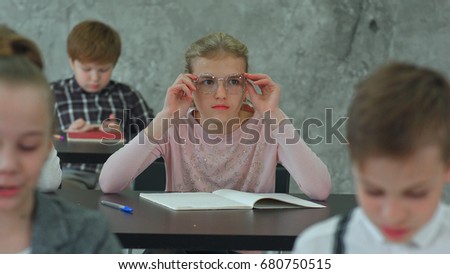 Schoolgirl putting on glasses during lesson