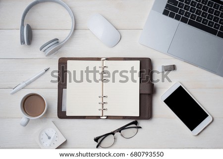 Top view on opened notebook, smartphone, laptop, eyeglasses, cup of coffee and other equipment on wooden office desk.