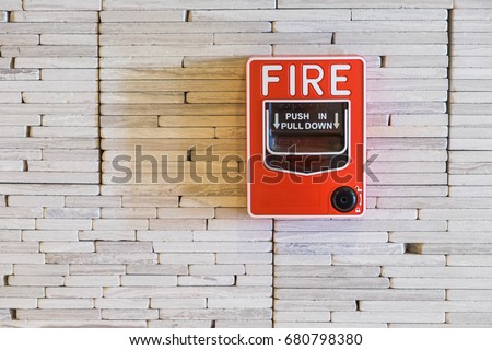 Fire alarm press button on white brick wall in the hotel corridor.