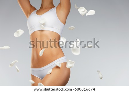 Woman Body Care. Closeup Of Beautiful Female Body In Shape With Fit Slim Figure, Healthy Smooth Soft Skin In White Bikini Panties With Flying White Flower Petals. Health Concept. High Resolution