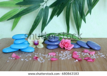 Decorative pebbles stacked in a Zen life fashion on a bamboo wooden board  with a pink flower and an orchid on a green and foliage background