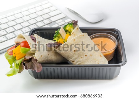 Salad box for take away (Pita bread wrapped with mixed vegetables) with thousand island dressing in plastic box have keyboard and mouse as blur background on white isolated, fast food  in busy day, Royalty-Free Stock Photo #680866933