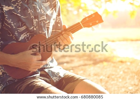 Closeup of young man hands playing acoustic guitar ukulele at the park sit Enjoy living Sunshine in the evening.   Royalty-Free Stock Photo #680880085