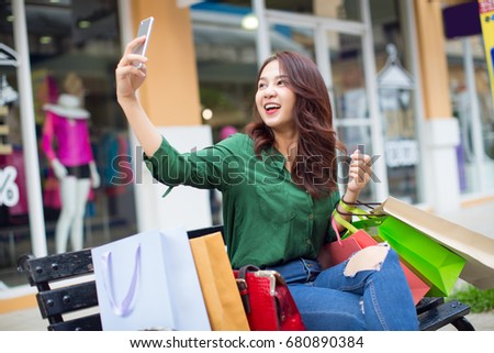 shopping Asia woman happy taking photo with smartphone. Woman holding shopping bags while taking self-portrait picture outdoor. multiracial Asian woman