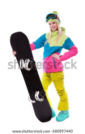 vertical picture, isolated on white, attractive  young caucasian girl in colorful ski costume, yellow trousers and blue ski glasses hold black snowboard, look at camera