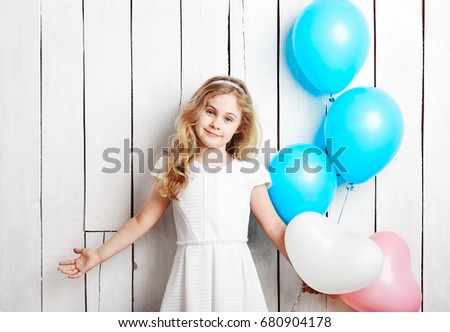 Cheerful little blonde girl with balloons on white wood backgrou