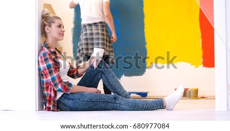 Happy couple doing home renovations, the man is painting the room and the woman is relaxing on the floor and drinking coffee