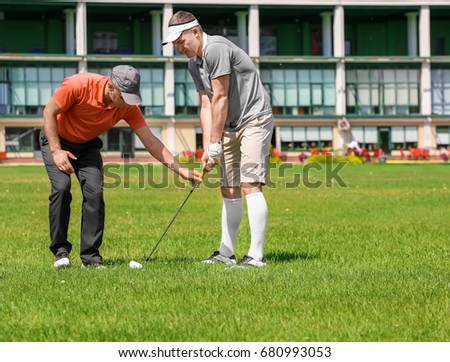 Caddy teaching young man to play golf on course in sunny day