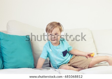 3 year old boy sits on the couch and listens to music. Little cute boy watching cartoons on the phone. Little boy.