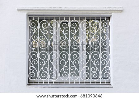 Window on the white wall. Figured frame of the window hole. Iron wrought-iron lattice curly painted white