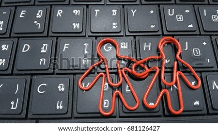 2 paper clips set position as 2 people holding hand together on the laptop keyboard background