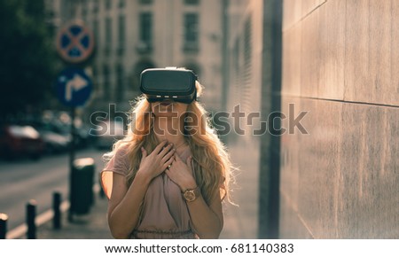 Blonde girl using cool VR set to experience living in fantasy computer game left amazing sights of the fantasy location Oculus VR technology VR gear Digital 3D video VR headset 360 video business