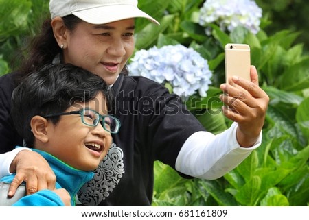 Happiness moment of grandchild and aunt smiling selfie in the park in warm day of spring season. Blurred background of Hydrangea shrub. Concept of happy family. Model release attached.