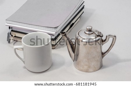 silver teapot and a white tea cup on a gray background with notebooks for records