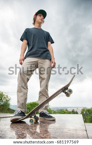 A young skater stands with a skateboard on the background of the landscape of the city