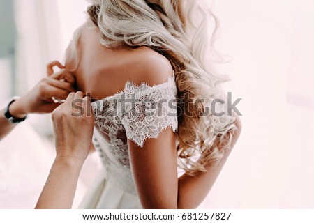 Gorgeous, blonde bride in white luxury dress is getting ready for wedding. Morning preparations. Woman putting on dress. Royalty-Free Stock Photo #681257827