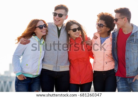 people, friendship and teenage concept - group of happy friends in sunglasses hugging and talking on city street