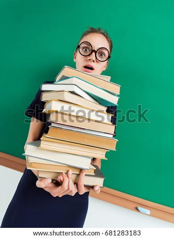 Astonished student with pile of books in her hands, staring at you with her mouth open. Photo of young girl wearing glasses. Back to school!