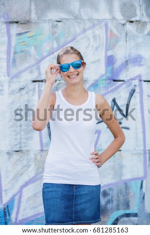 Hipster girl wearing blank white t-shirt, jeans and sunglasses posing against rough street wall, minimalist urban clothing style, mockup for tshirt print store