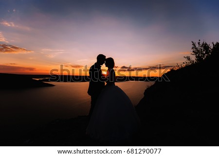 Silhouette of embracing groom and bride. Tenderly kissing wedding couple on an orange sunset