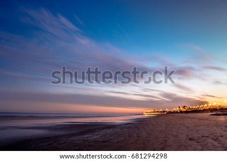 Sunset over a beach with city lightnings at the background.