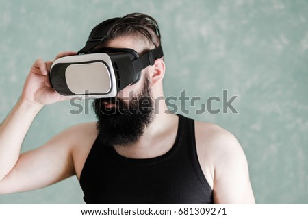 Young bearded man in black t-shirt and VR glasses looking impressed, isolated on green background.