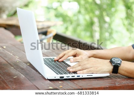 Close up low angle view of a man working on a laptop computer sitting on wooden table with blur nature background