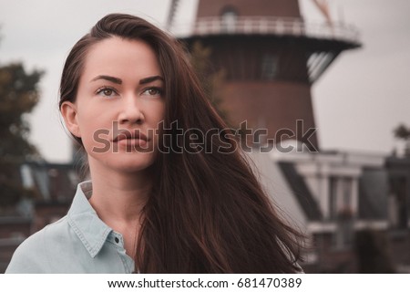 Beautiful brown hair young Caucasian model girl wearing a buttoned shirt posing on a outside terrace in Utrecht, The Netherlands with windmill at the background