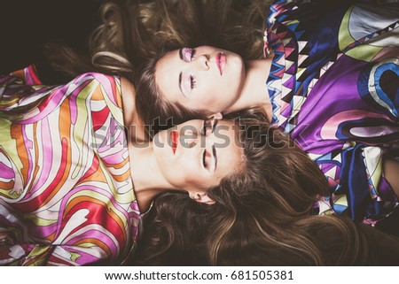 beautiful two young women with long blonde hair beauty fashion portrait lie down in colorful silky dress studio shot