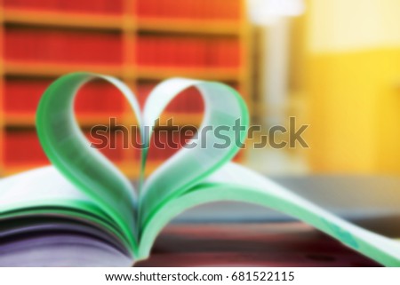 Heart shape of paper on table in library with red books on shelf in the background , blurred effect