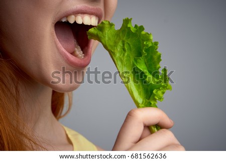 Woman eating lettuce leaves on gray background close-up diet                               