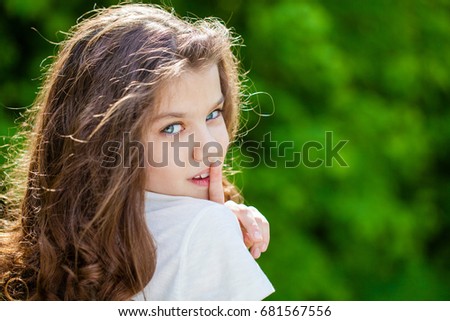 Young beautiful Little girl has put forefinger to lips as sign of silence, outdoors summer