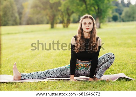 Young sports woman doing yoga exercises outdoors on green lawn at the sunset