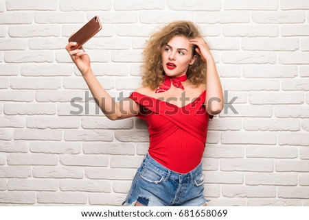 Girl taking selfie smart phone camera excited happy smile woman over white brick office wall