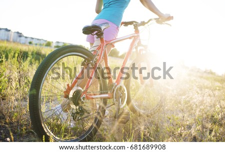 Beautiful young woman walking with a bicycle at sunset