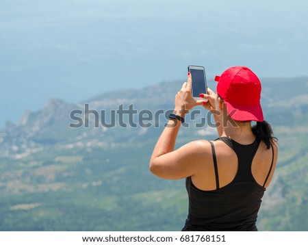 Successful sport woman backpacker treveller with baseball cap use smartphone taking photographs on seaside high mountain rock