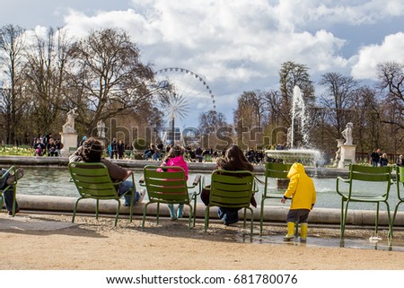 little boy in yellow rain jacket playing in puddle in front of fountain on place de la concorde paris with ferris wheel in background