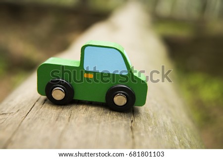 green wooden Car toy stand on tree trunk in perspective. car in forest