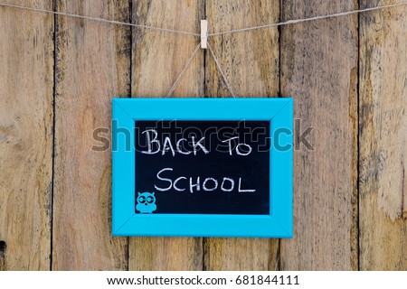 Back to School hand written in chalk on blackboard with blue frame hanging against old rustic timber wooden background - with owl shape