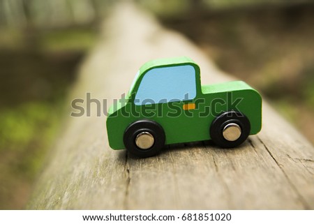 green wooden Car toy stand on tree trunk in perspective. car in forest